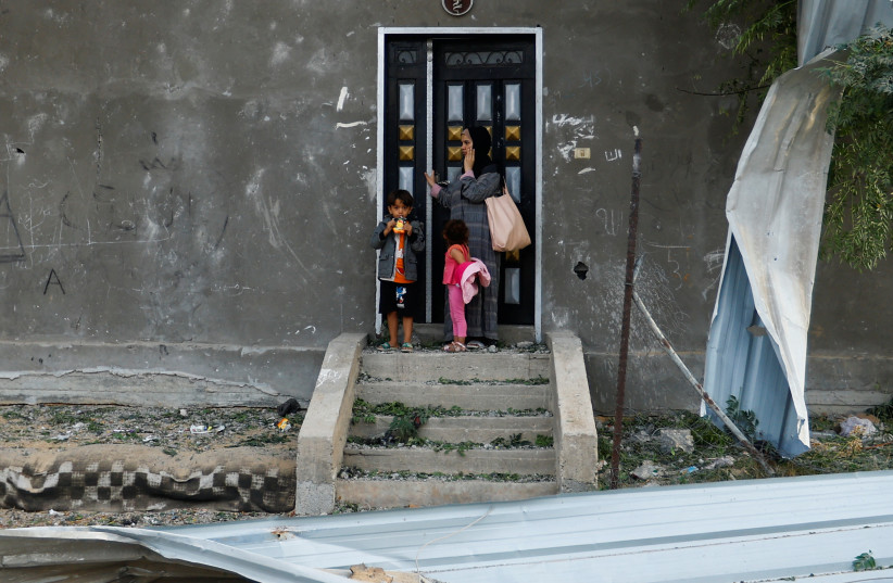  A Palestinian woman stands with children at the door of a damaged house, following Israeli strikes, in Khan Younis in the southern Gaza Strip October 11, 2023. (credit: IBRAHEEM ABU MUSTAFA/REUTERS)