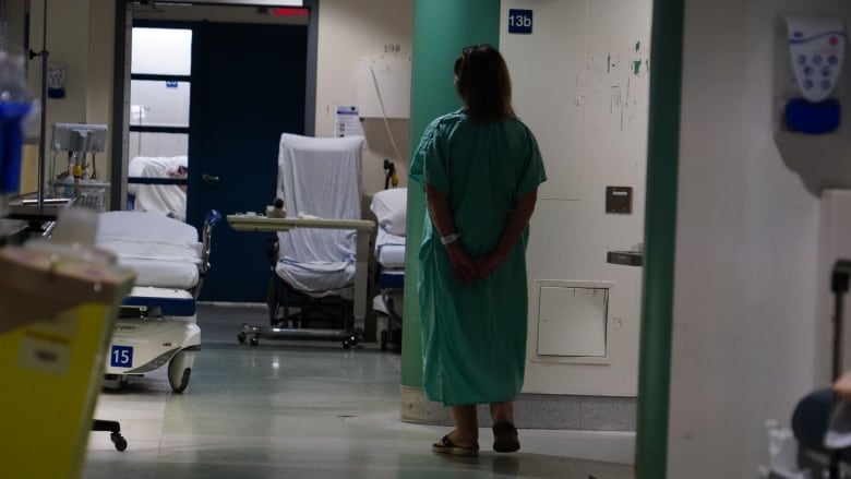 A woman in a hospital gown stands in a hallway